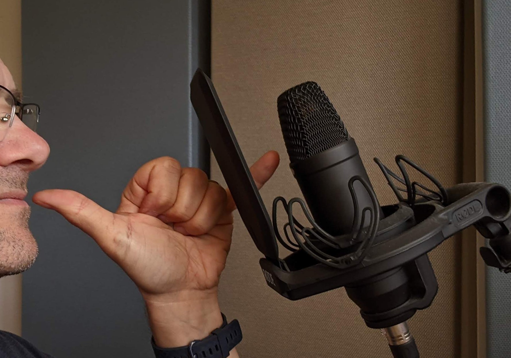 Man with thumb touching lips, pinkie touching microphone, other fingers curled